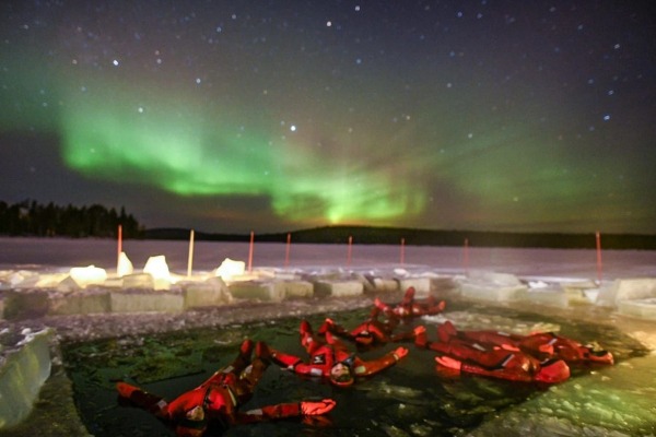 Grupo de pessoas em trajes especiais flutuando em um pequeno lago enquanto observam a aurora boreal na Lapônia.