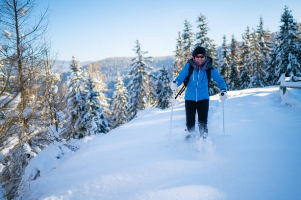 Homem com raquetes de neve e bastões de trekking passando por uma floresta íngreme coberta de neve