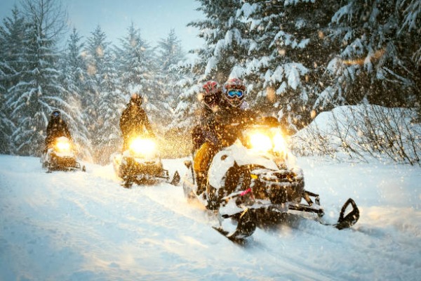 Pessoas em motos de neve andando em trilhas com neve e com neve ao mesmo tempo