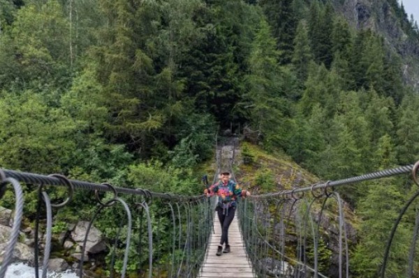 Mulher em uma ponte suspensa com vegetação ao fundo