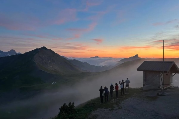 Pessoas assistindo ao pôr do sol no topo de uma montanha com vista para o Mont Blanc