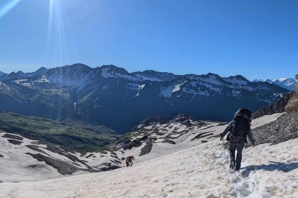 Alpinistas passando por montanhas cobertas de neve com uma paisagem ensolarada