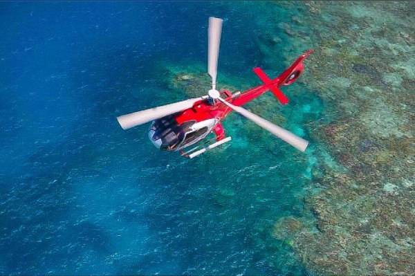 Vista aérea de um helicóptero vermelho sobrevoando a Grande Barreira de Corais Vista aérea panorâmica de um helicóptero vermelho sobrevoando as águas azul-turquesa do recife de corais em Cairns.