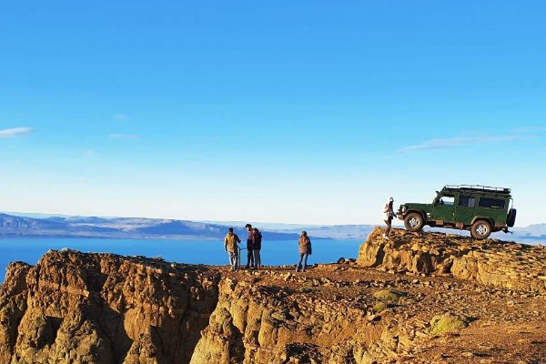 Mirante no penhasco com vista panorâmica para o Lago Argentino Grupo de pessoas e veículo 4x4 no topo de um penhasco rochoso com vista para o lago.