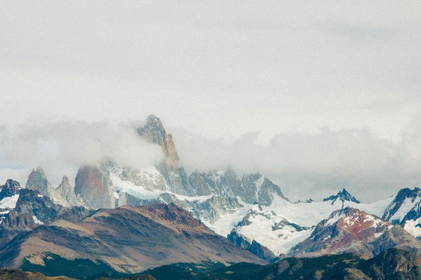 estrada com grama nas laterais e montanhas cobertas de neve ao fundo