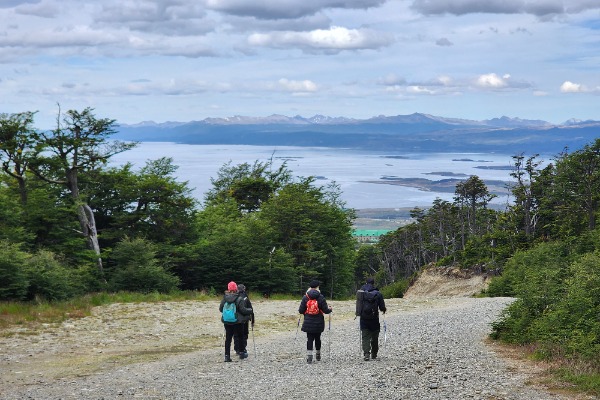 Pessoas descendo um terreno rochoso com vista para a cidade de Ushuaia