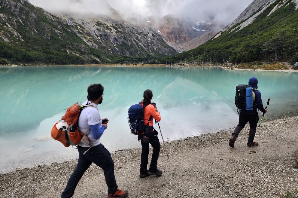 três pessoas equipadas com bastões de trekking caminhando ao lado da lagoa Esmeralda