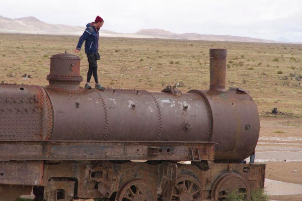 Viajante caminhando em cima de um trem velho e abandonado no cemitério de trens de Uyuni