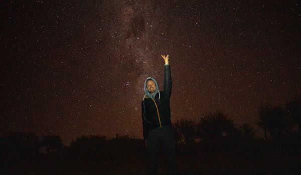 Tour de observação de estrelas menino com o braço levantado contra o pano de fundo do céu estrelado