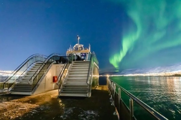 Segeln auf der Suche nach Polarlichtern Schiff auf See mit Polarlicht im Vordergrund und schneebedeckter Landschaft