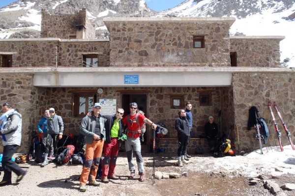 Die Toubkal-Hütte im Hohen Atlas, wo sich Bergsteiger auf den Aufstieg vorbereiten Eine Gruppe von Wanderern am Eingang zur Toubkal-Hütte im Hohen Atlas, umgeben von Schnee und hohen Bergen
