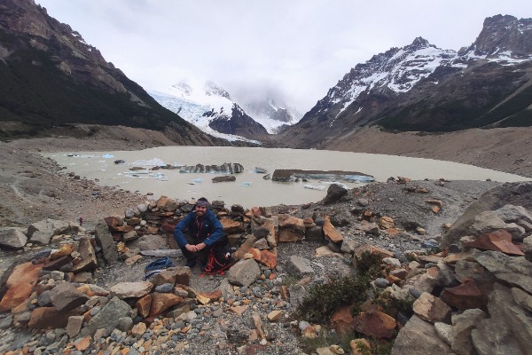 Reisende in der Torre-Lagune mit Blick auf den Cerro Torre Eine Person sitzt vor der Laguna Torre mit Eisschollen und schneebedeckten Bergen im Hintergrund in El Chalten.