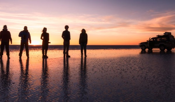 Zugang zu den Salinen von Uyuni gruppe von reisenden in den salzebenen von uyuni bei sonnenuntergang mit ihrem 4x4-fahrzeug