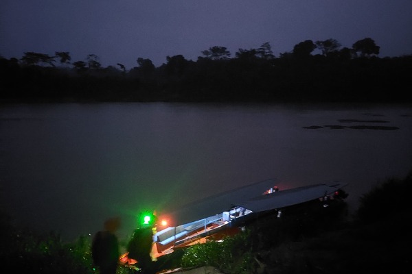Nachtwanderung entlang des Flusses Madre de Dios Beleuchtetes Boot mit Touristen während einer Nachtsafari auf dem Madre de Dios-Fluss in Puerto Maldonado.