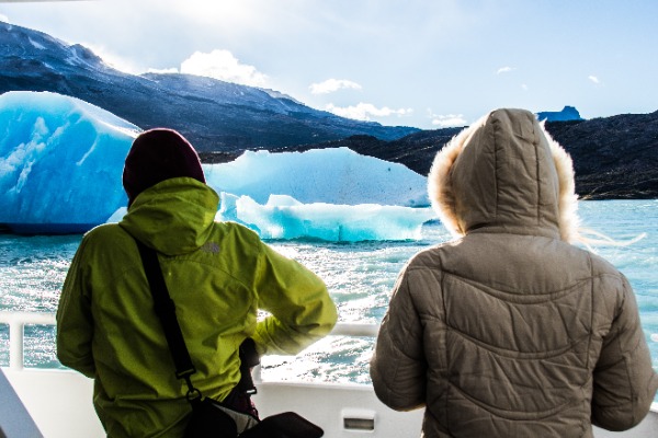 people facing away taking photos of iceberg during navigation