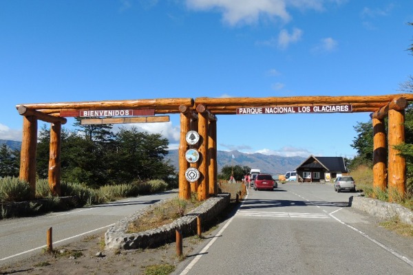 Wooden entrance with a welcome sign to Los Glaciares National Park and parked cars in the background