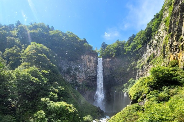 The Stunning Kegon Falls on the Nikko Day Trip from Tokyo A large waterfall cascading vertically down between lush green mountains under a clear sky.