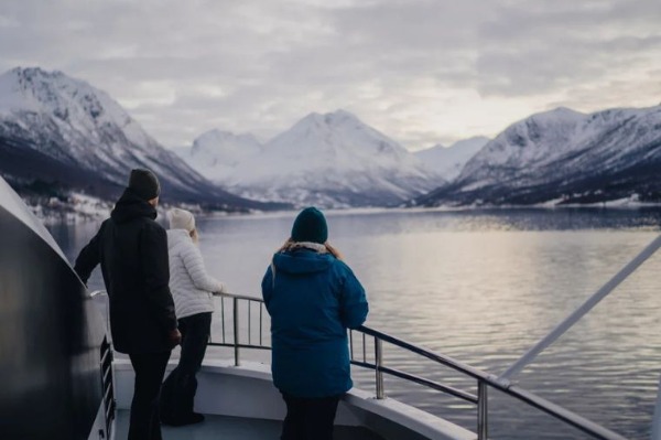 people in warm clothes looking at the snowy arctic fjord landscape from the boat