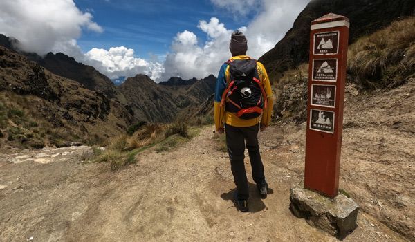 traveler howlanders next to the Abra Warmiwañusca pass sign inca trail