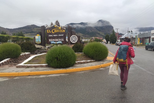 Llegada a El Chaltén, capital del trekking Viajera caminando hacia el cartel de bienvenida a El Chaltén, bajo un cielo nublado