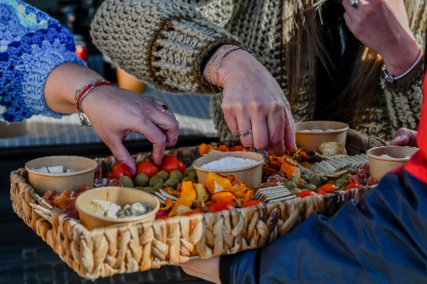 Aperitivos gourmet preparados durante el Torres del Paine Puma Tour – Safari Privado Bandeja de mimbre con aperitivos de queso, aceitunas, tomates y snacks servidos al aire libre.