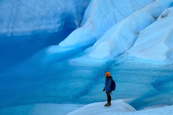 Excursionista con crampones caminando sobre el Glaciar Grey junto a una laguna azul en Torres del Paine