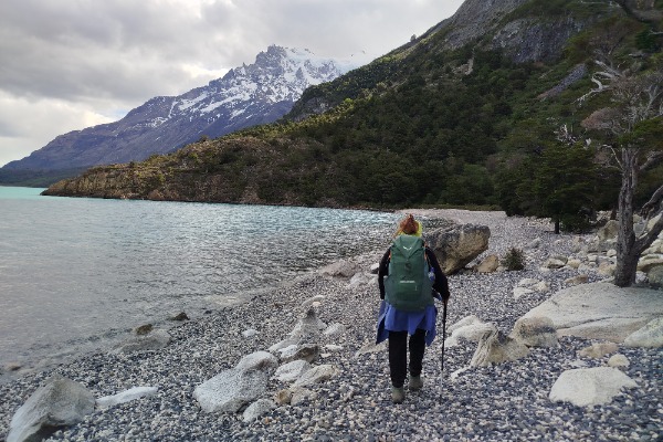 Senderista caminando por la orilla del Lago Nordenskjöld con montañas nevadas al fondo