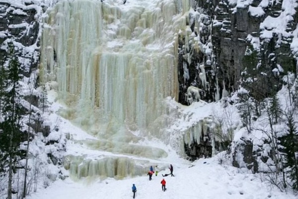 Personas en la nieve frente a la cascada congelada de Korouoma