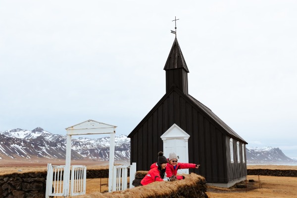 Iglesia negra con turistas viéndola por fuera y montañas nevadas de fondo
