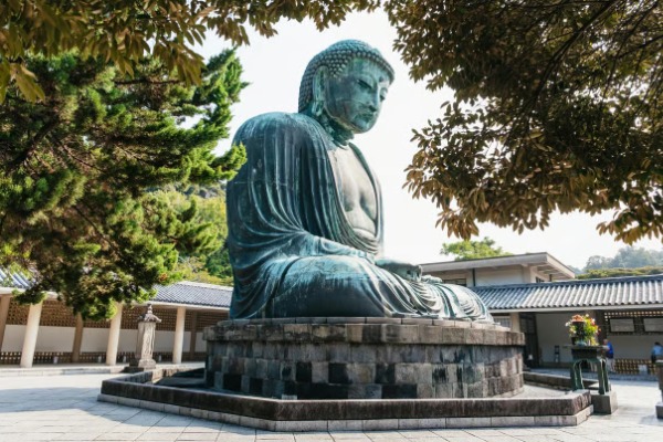 Estatua monumental del Gran Buda de Kamakura en la Excursión a Kamakura y Hakone desde Tokio Gran estatua de bronce del Buda sentado en el templo Kotoku-in vista de perfil bajo la sombra de los árboles.