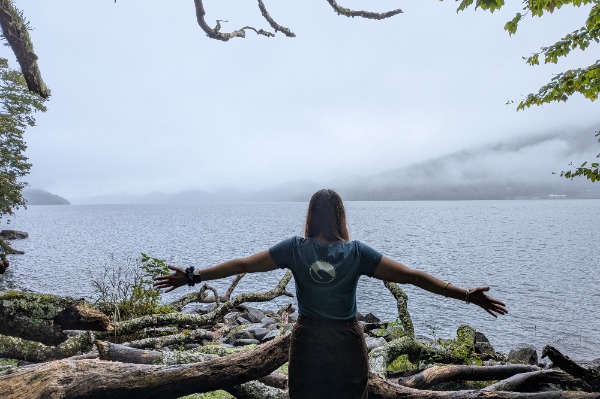 Panorámica del lago Chuzenji entre la niebla durante la Excursión a Nikko desde Tokio Mujer con los brazos abiertos contemplando la tranquilidad del lago Chuzenji rodeado de troncos y montañas con niebla.