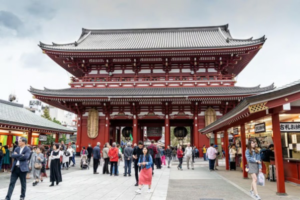 Visitantes caminando frente a la majestuosa puerta roja Hozomon en el complejo del templo Senso-ji.
