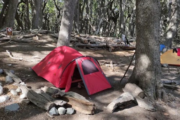 Tente au Camp Poincenot Tente rouge installée dans le camp de Poincenot parmi les arbres et les troncs.