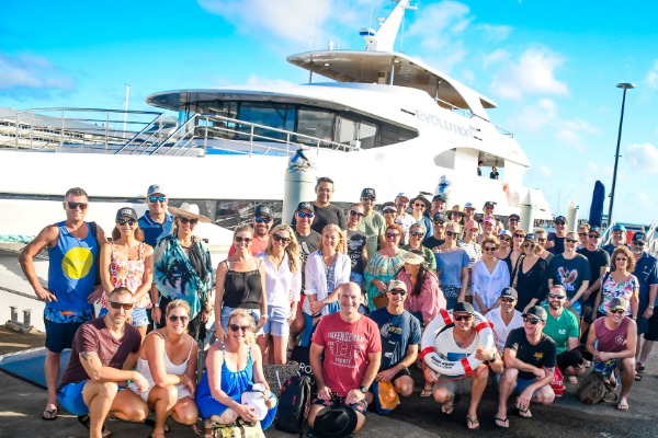 Un groupe de passagers avant d'embarquer pour une excursion en semi-submersible le long de la barrière de corail au départ de Cairns Un grand groupe de touristes posant devant le catamaran Evolution dans le port de Cairns.
