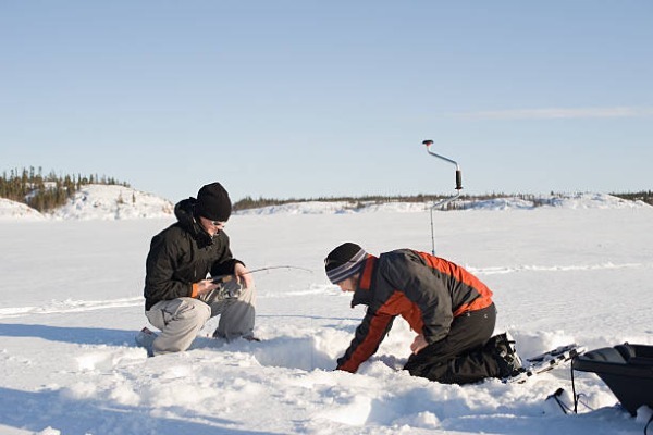 pêche sur glace à Rovaniemi deux personnes accroupies sur la glace pêchant dans un trou fait dans la glace
