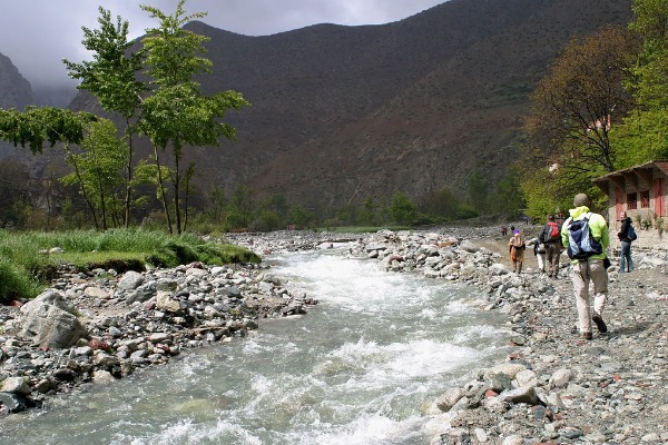 Itinerario attraverso i villaggi berberi dell'Alto Atlante Escursionisti che camminano lungo un fiume di montagna durante l'itinerario attraverso i villaggi berberi dell'Alto Atlante in Marocco.