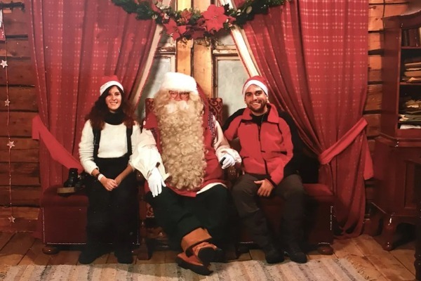 Un bambino e una bambina siedono accanto a Babbo Natale nella sua casa di legno.