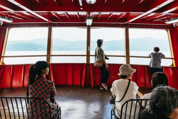Passeggeri che ammirano il lago Ashi dal ponte dell'imbarcazione durante l'escursione a Kamakura e Hakone da Tokyo Turisti che ammirano il panorama del lago Ashi attraverso i finestrini di un battello turistico.